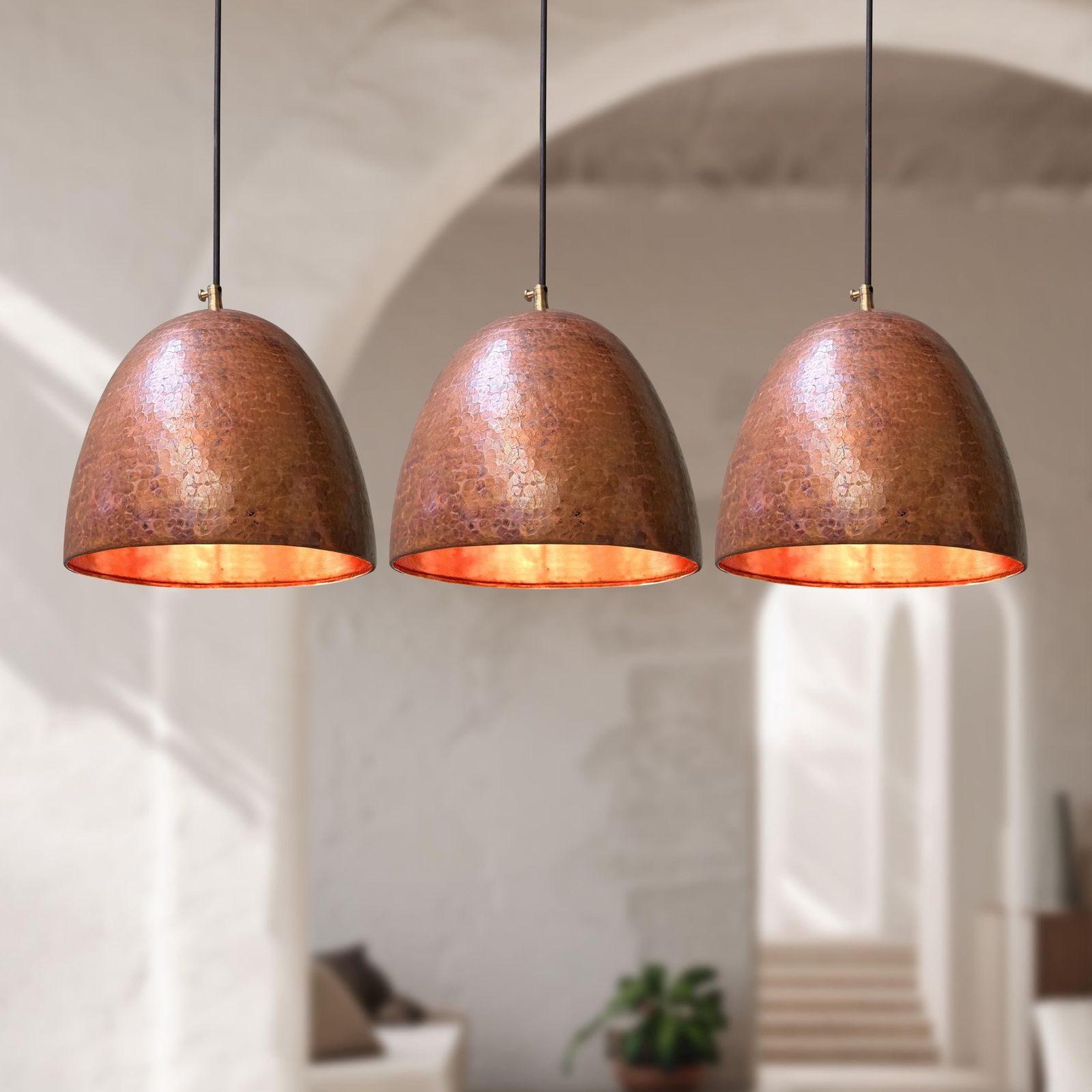 Three copper pendant lights hanging in a room with a blurred background