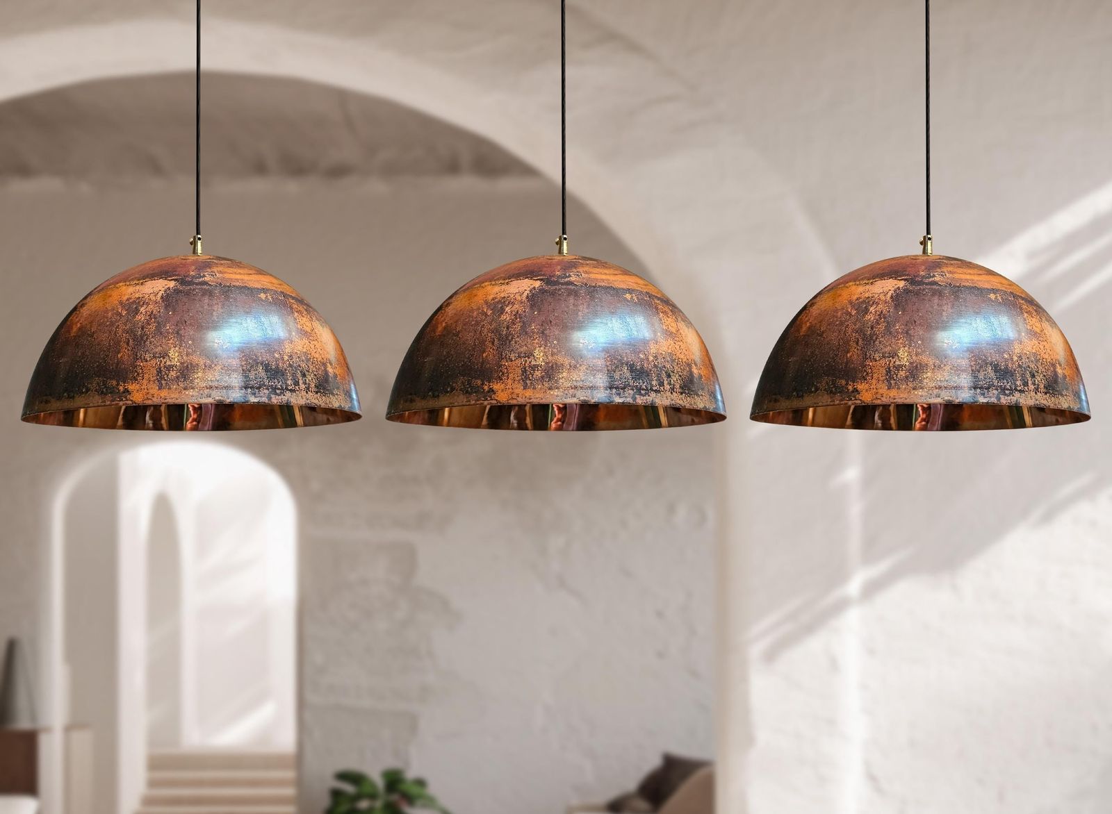 Three dome-shaped pendant lights with distressed copper and bronze metallic finishes hanging in a softly lit interior with arched walls.