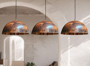 Three dome-shaped pendant lights with distressed copper and bronze metallic finishes hanging in a softly lit interior with arched walls.