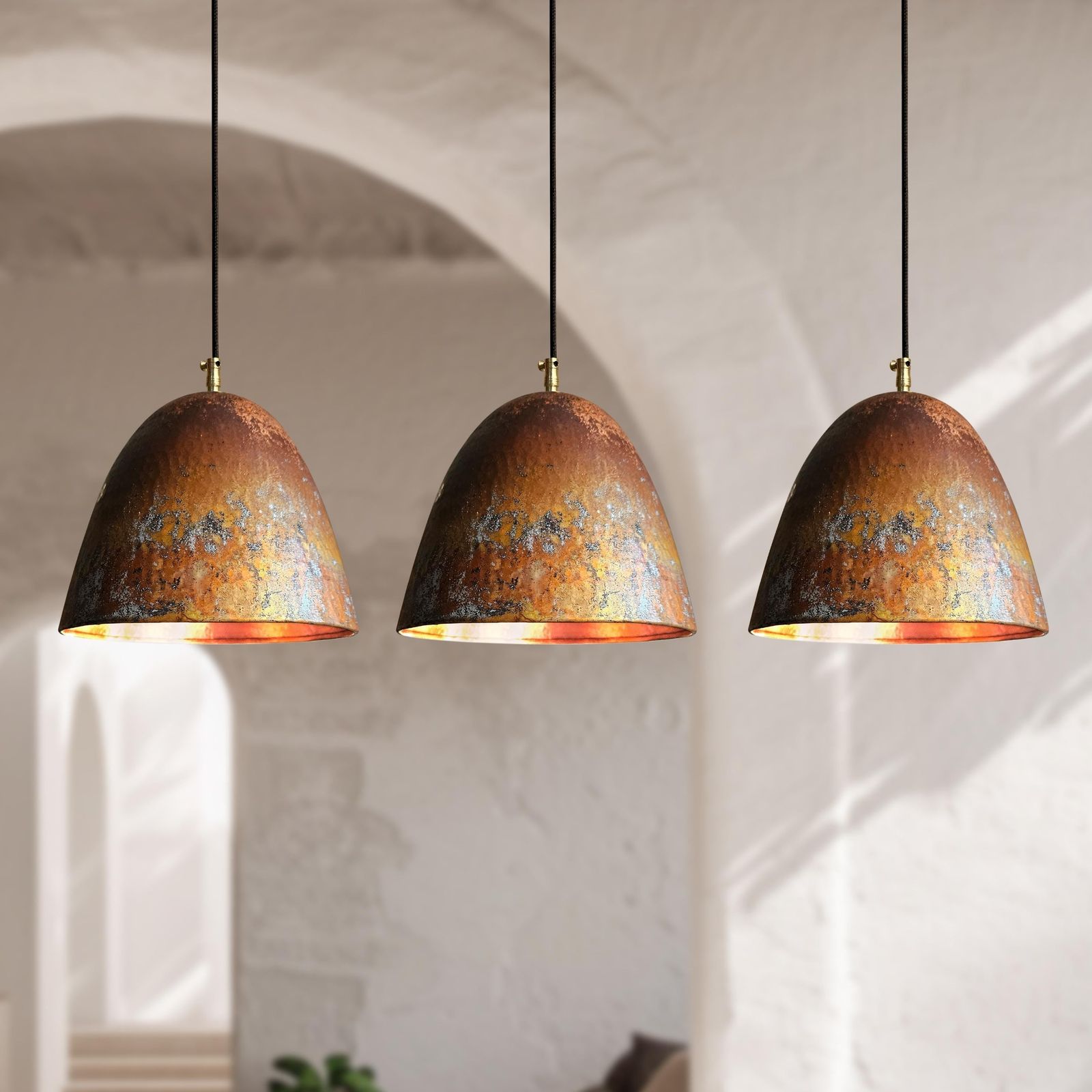 Three matching dome-shaped pendant lights with textured copper and gold metallic shades hanging in a row against a softly blurred white archway interior.