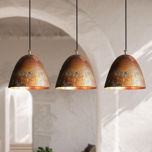 Three matching dome-shaped pendant lights with textured copper and gold metallic shades hanging in a row against a softly blurred white archway interior.