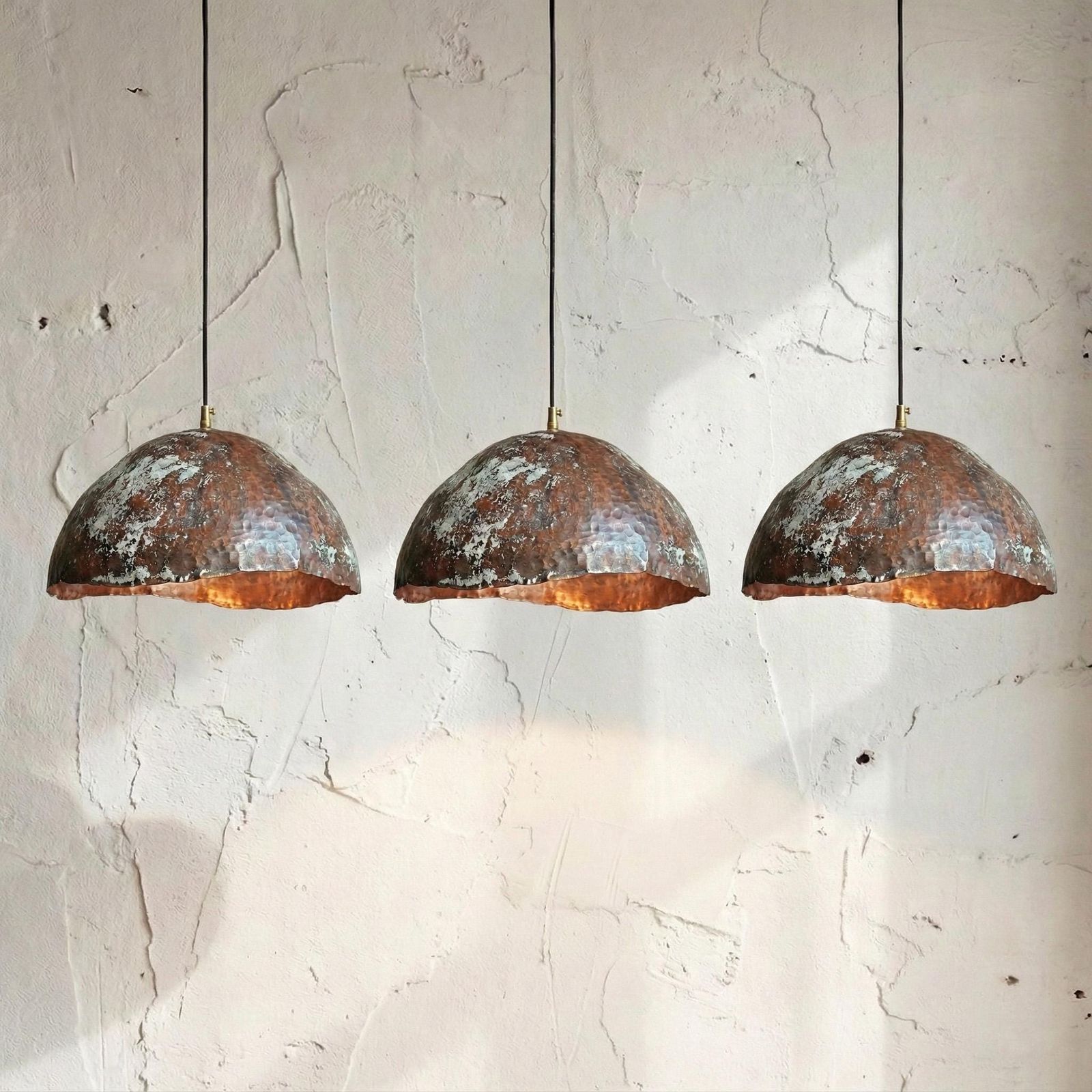 Three rustic copper dome pendant lights hanging side by side against a textured off-white plaster wall.