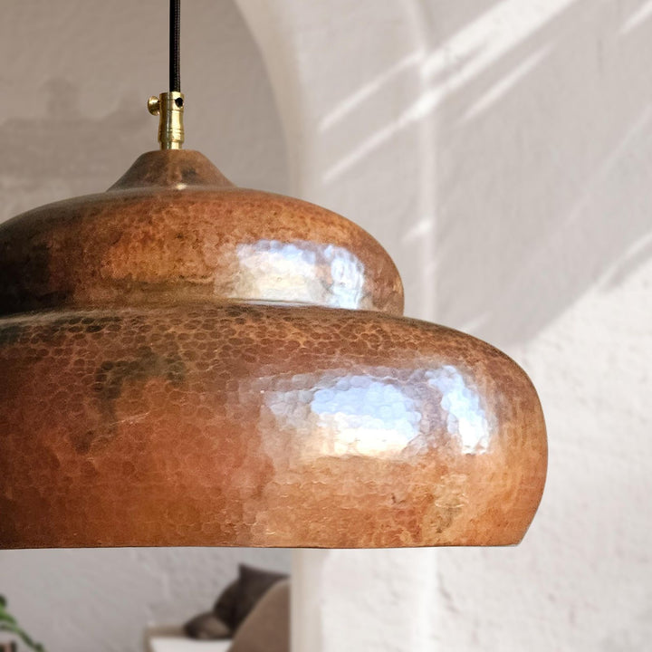 Close-up of a copper pendant light with a textured finish against a neutral background