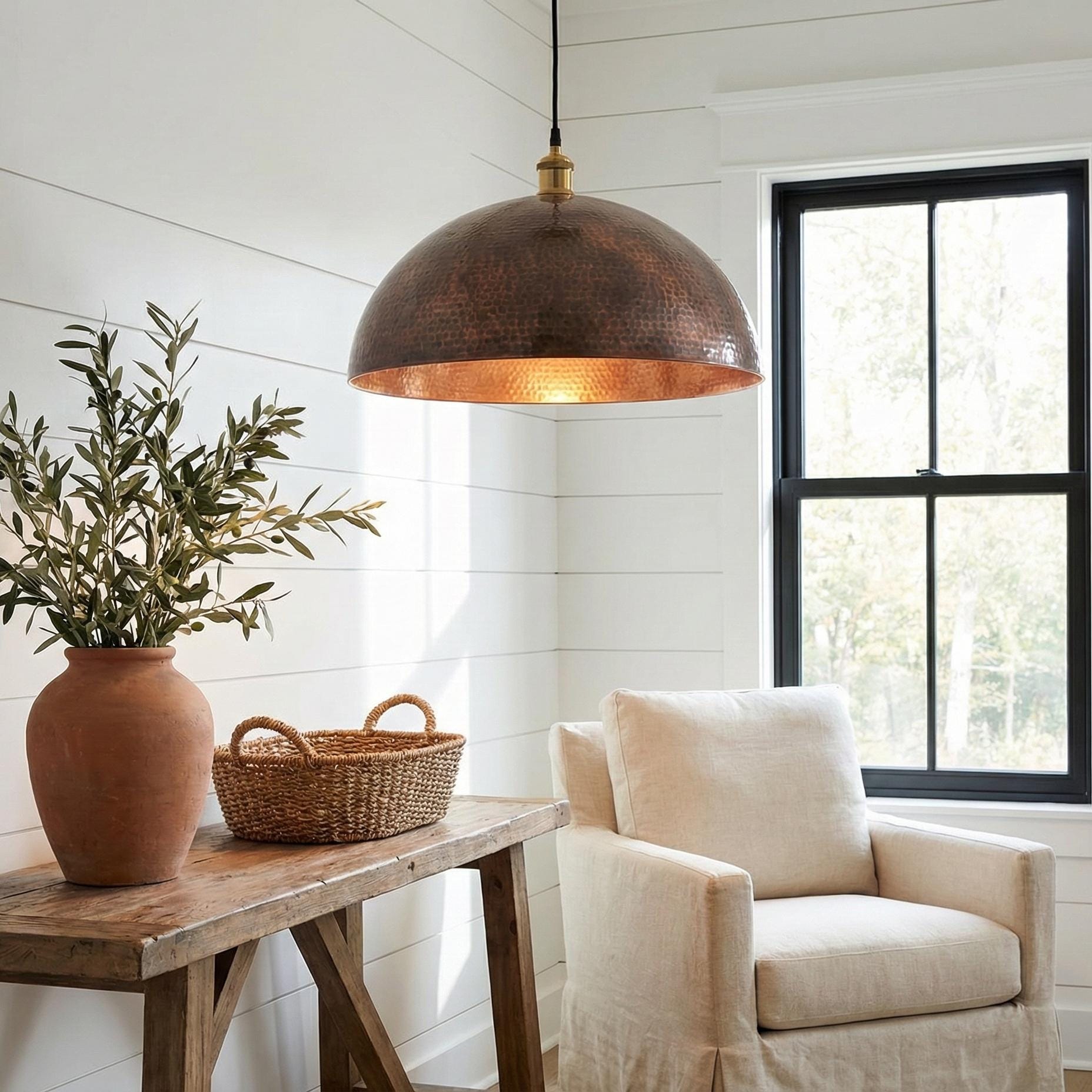 Cozy living room with a wooden table, potted plant, wicker basket, and beige armchair under a copper pendant light.