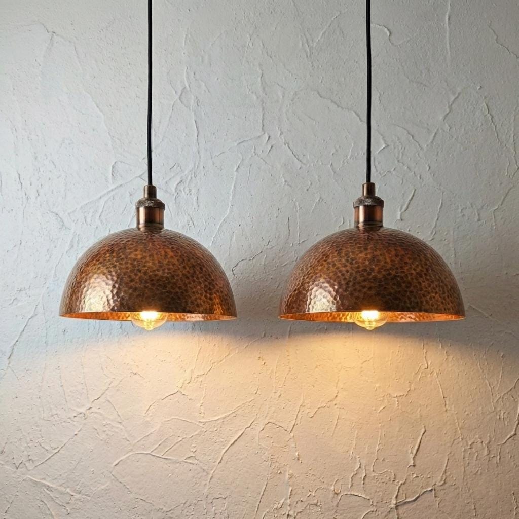 Two copper pendant lights hanging against a textured white wall.