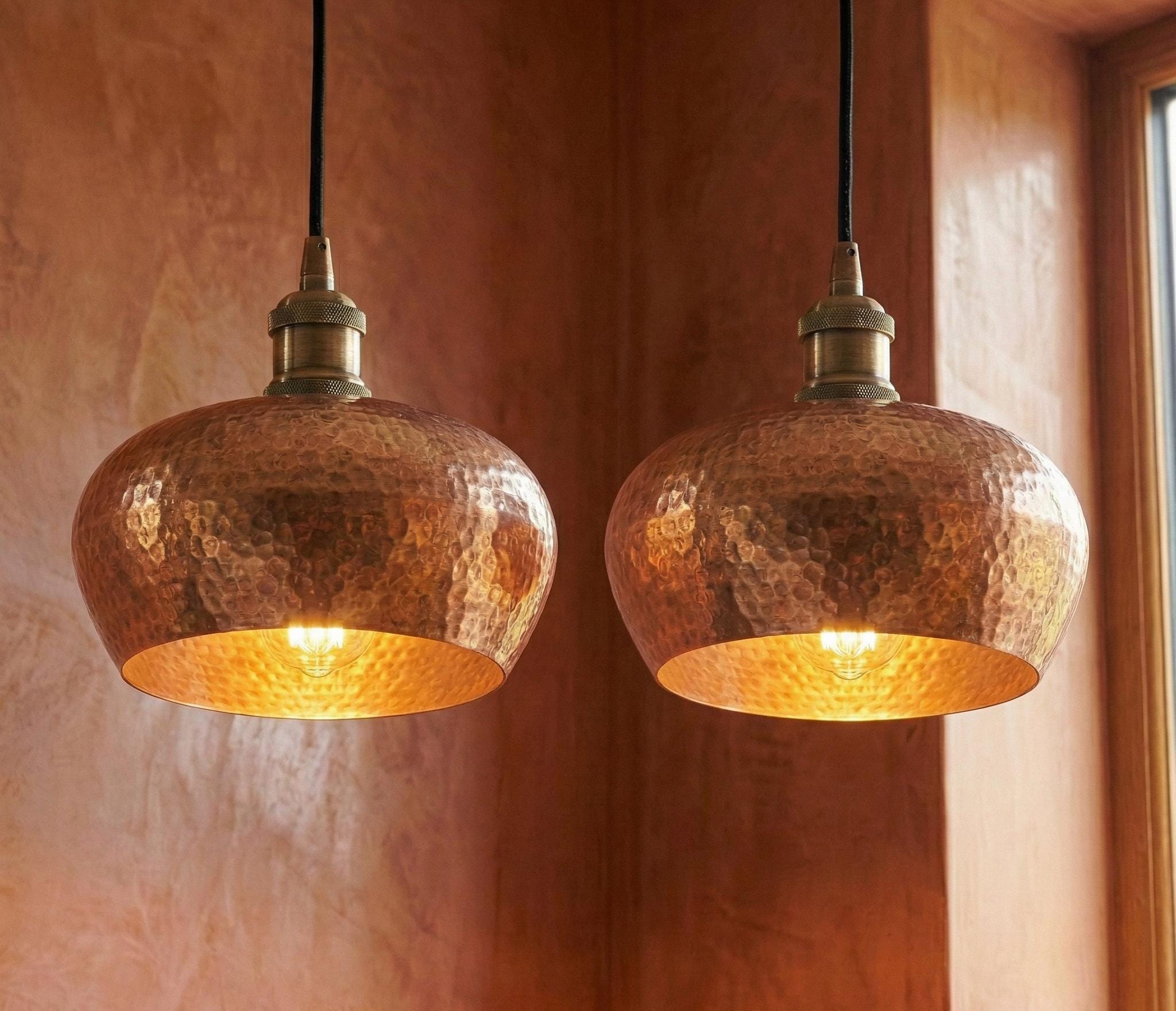 Two copper pendant lights hanging against a warm-toned wall.