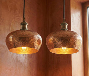 Two copper pendant lights hanging against a warm-toned wall.