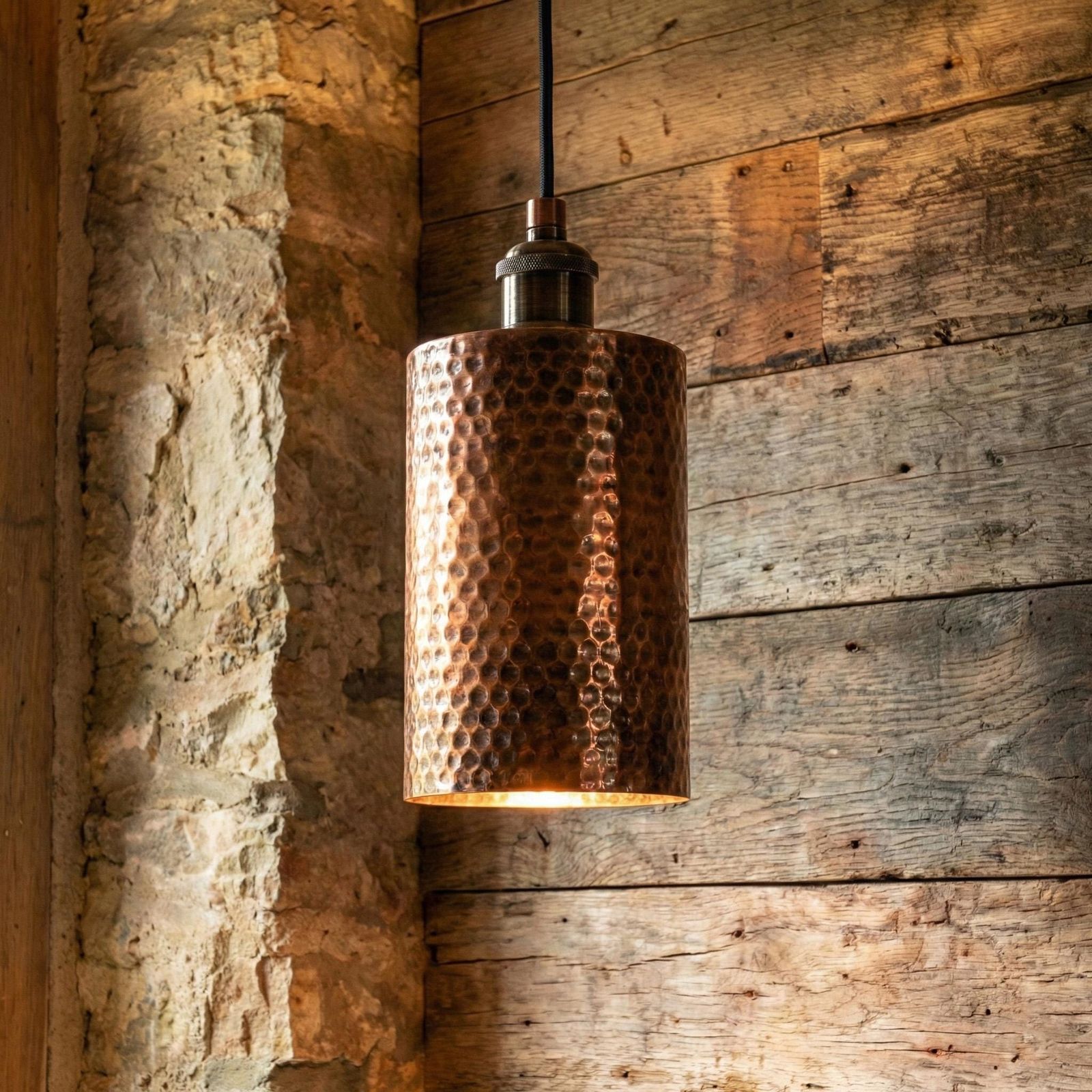 Copper pendant light hanging against a rustic wooden wall.