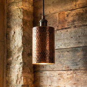 Copper pendant light hanging against a rustic wooden wall.