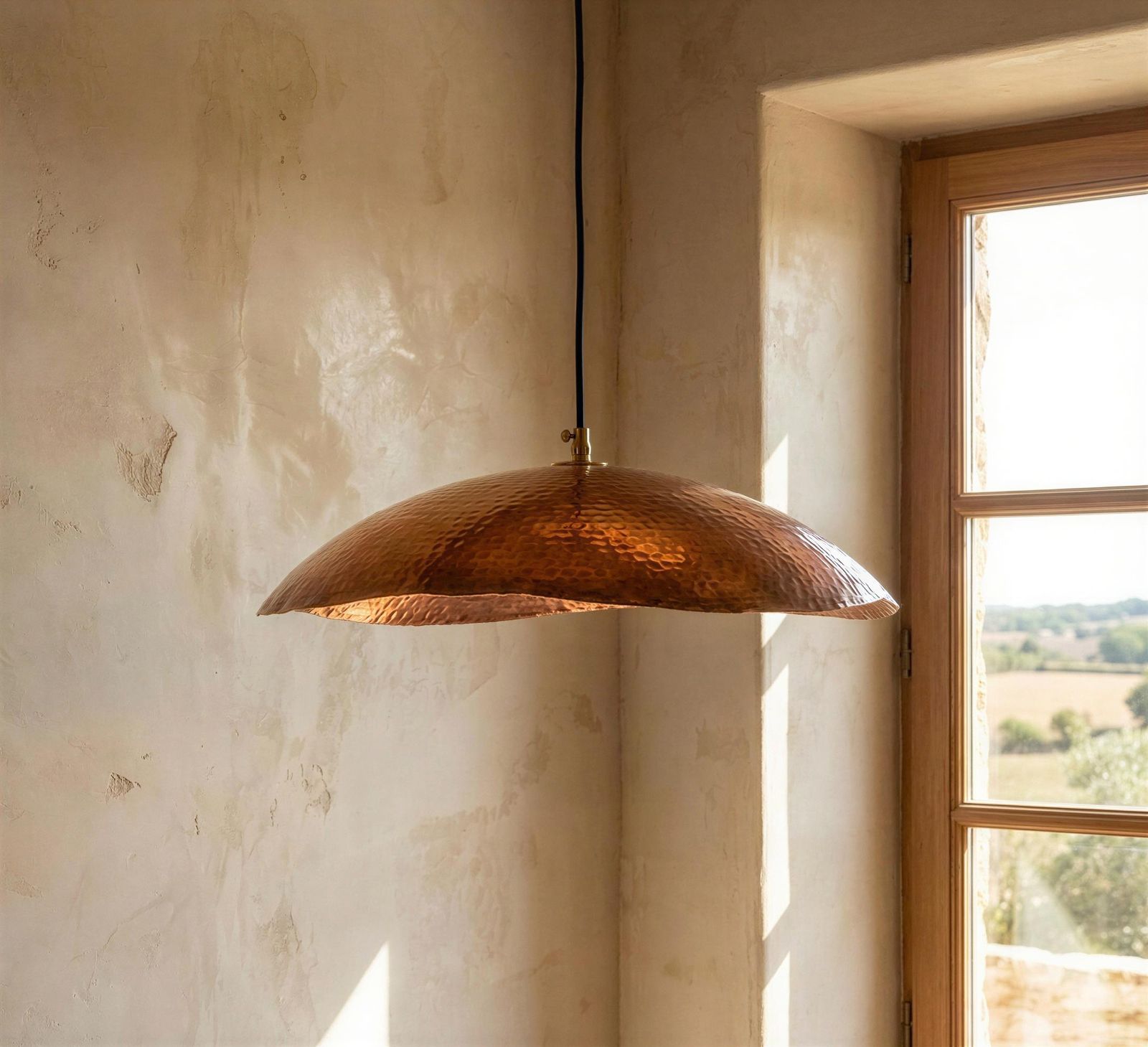 Copper pendant light hanging in a room with a window showing a view of trees.