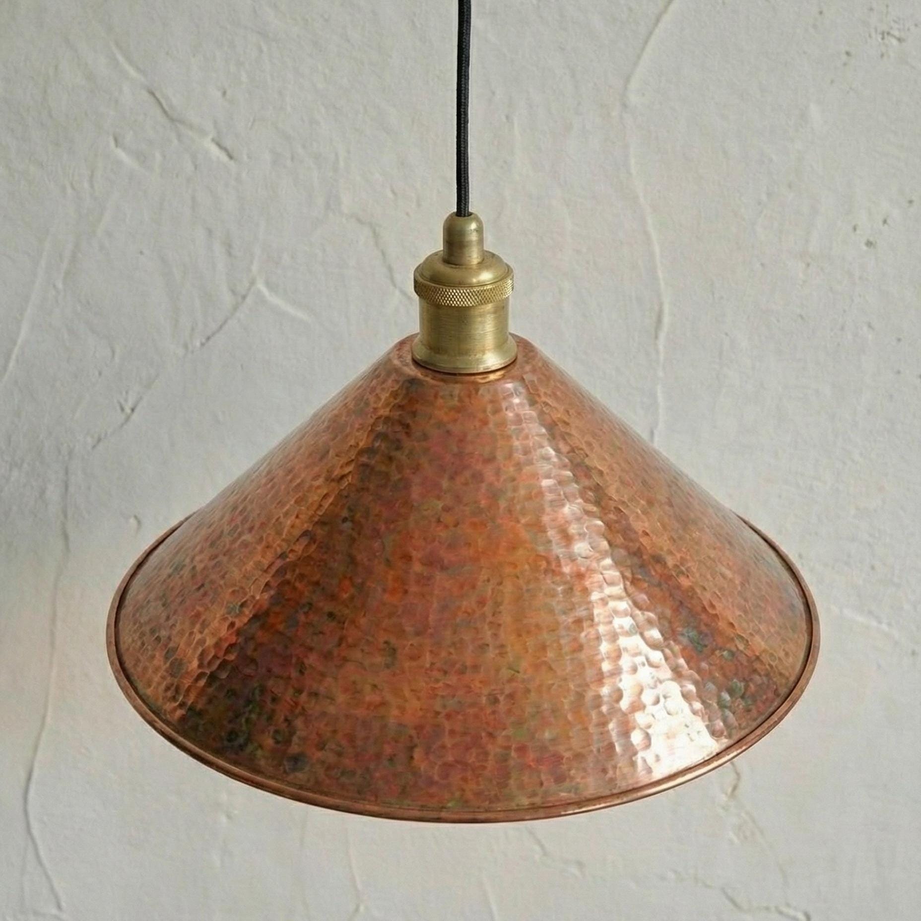 Copper pendant light with brass fitting against a textured white wall