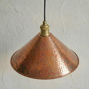 Copper pendant light with brass fitting against a textured white wall
