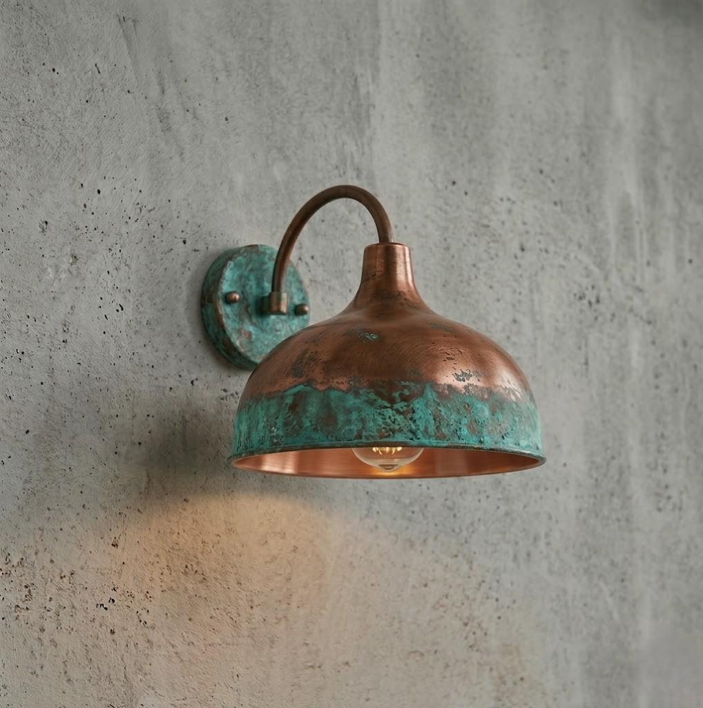 A vintage-style industrial wall sconce with a hammered copper dome shade and a turquoise verdigris patina, mounted on a textured gray concrete wall and casting a warm light downward.