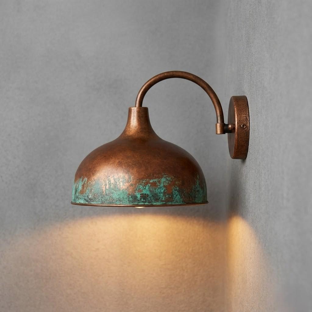 A vintage-style copper dome wall sconce with a distressed green patina and warm amber glow, mounted on a textured gray wall.