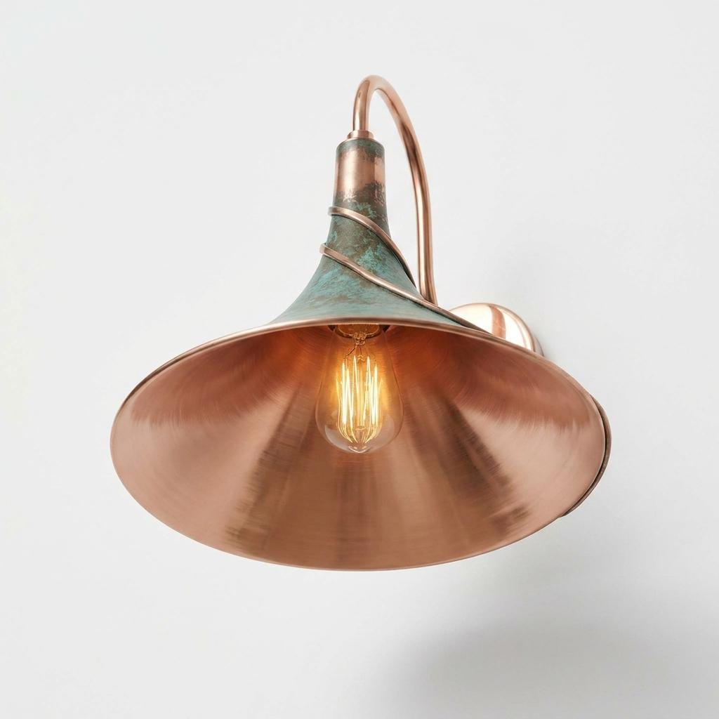 A vintage-style industrial wall sconce featuring a large copper-colored metal shade, a curved copper arm, and a textured greenish-bronze collar with a glowing filament bulb inside, set against a plain light gray background.