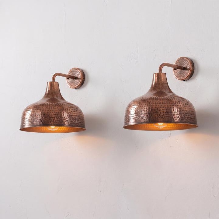 Two matching hammered copper wall sconces with warm glowing bulbs, mounted on a light gray textured wall.