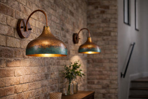Two copper wall sconces with hammered metal shades and a teal-blue patina finish, mounted on a rustic brick wall in a warmly lit interior.