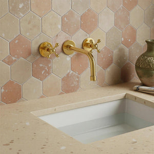 Gold faucet on a tiled wall with a sink below