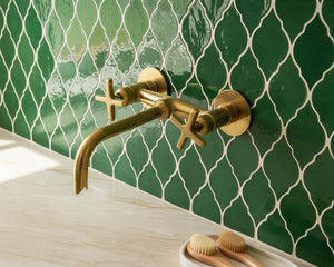 Gold faucet on a green tiled wall with a wooden surface and toothbrushes below.