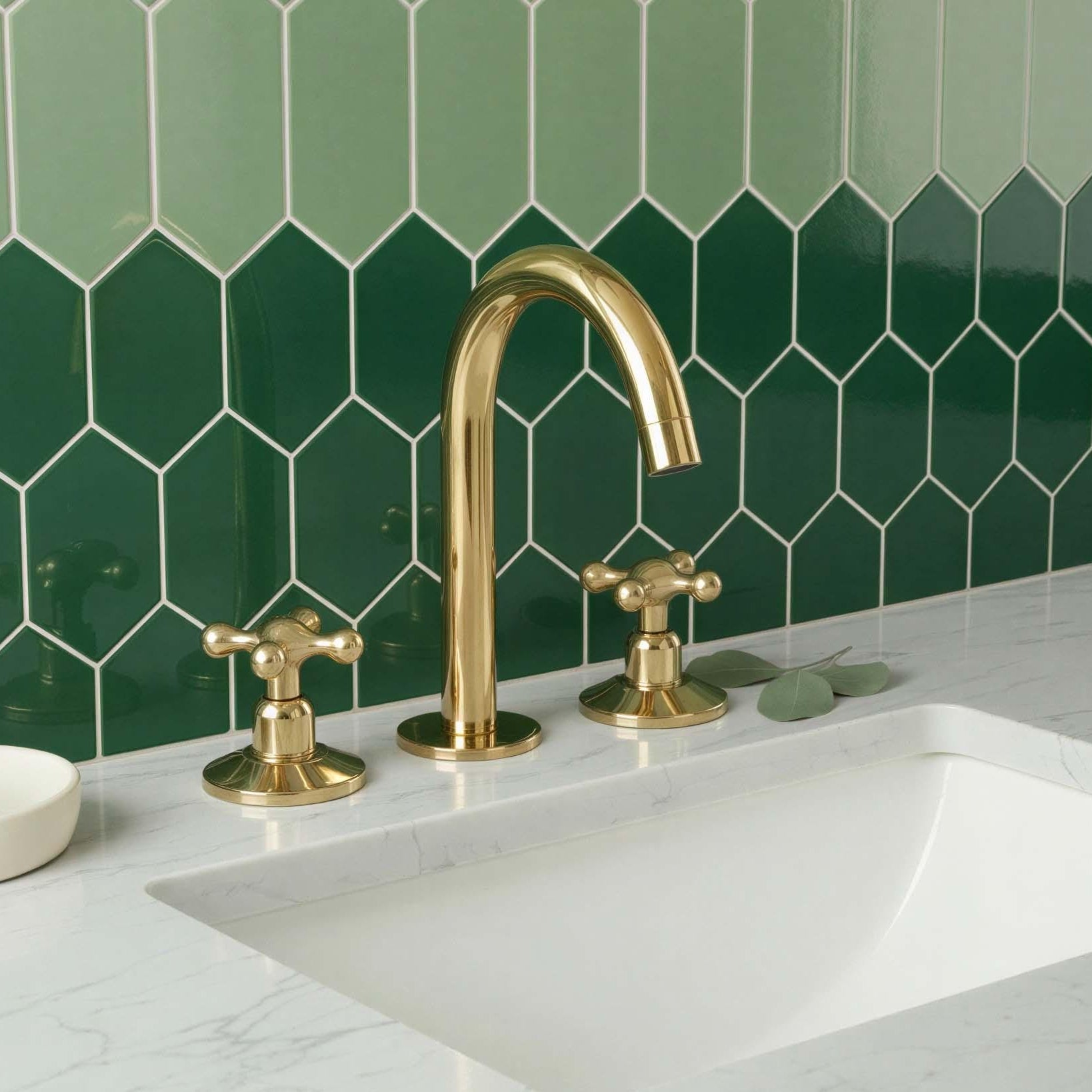 Gold faucet and handles on a white sink with green tiled wall
