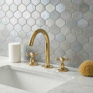Gold faucet and handles on a white sink with hexagonal gray tiles in the background