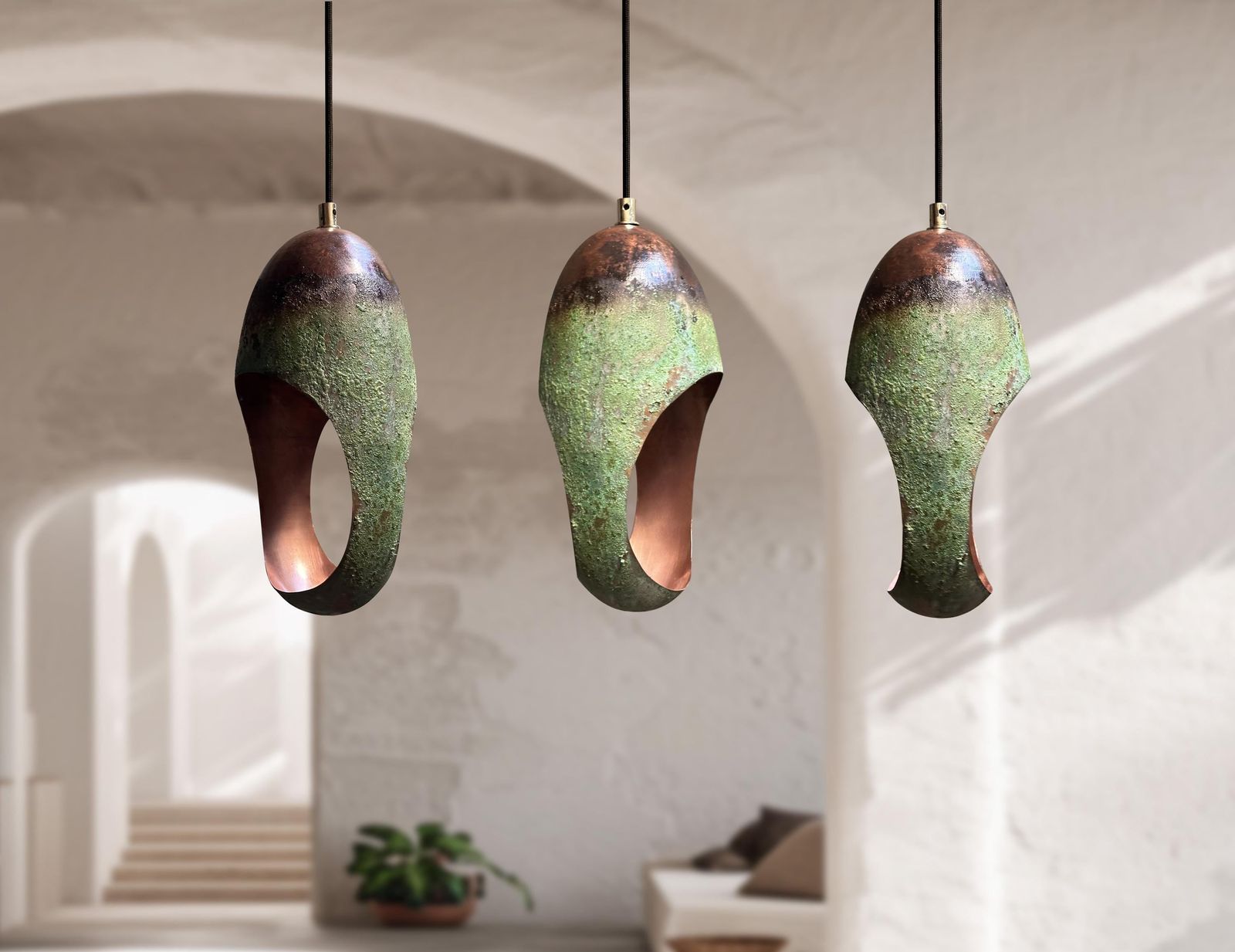 Three hanging pendant lights with organic teardrop shapes, featuring a textured green and brown ceramic-like finish with a copper-toned interior, suspended in a softly blurred modern interior setting.