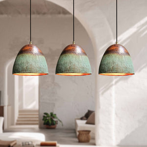 Three matching pendant light fixtures with textured green and copper-colored dome shades hanging in a bright, modern room with white arches and soft sunlight.