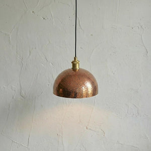 Copper pendant light hanging against a textured white wall