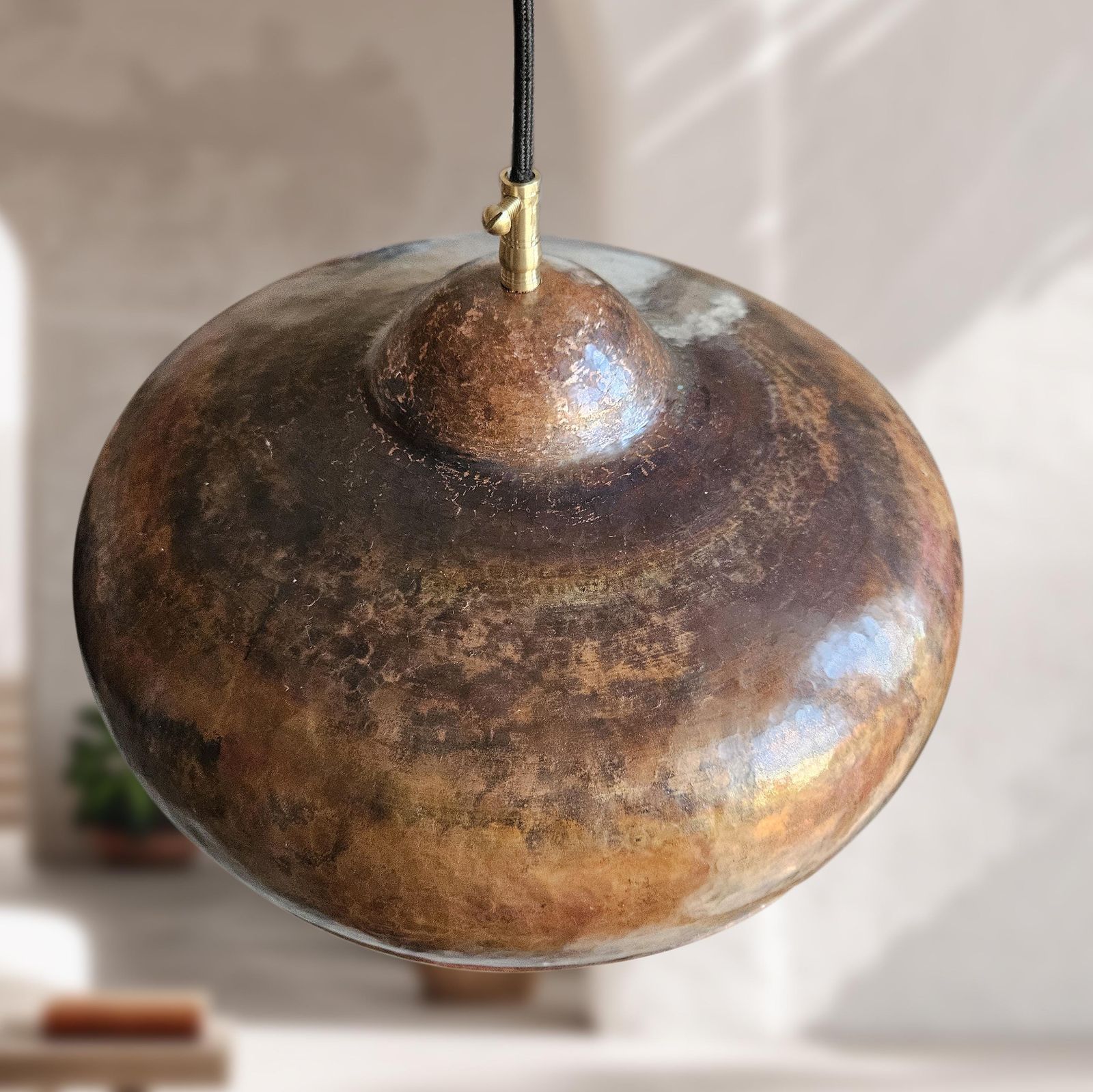 Decorative pendant light with a textured, metallic finish on a blurred indoor background