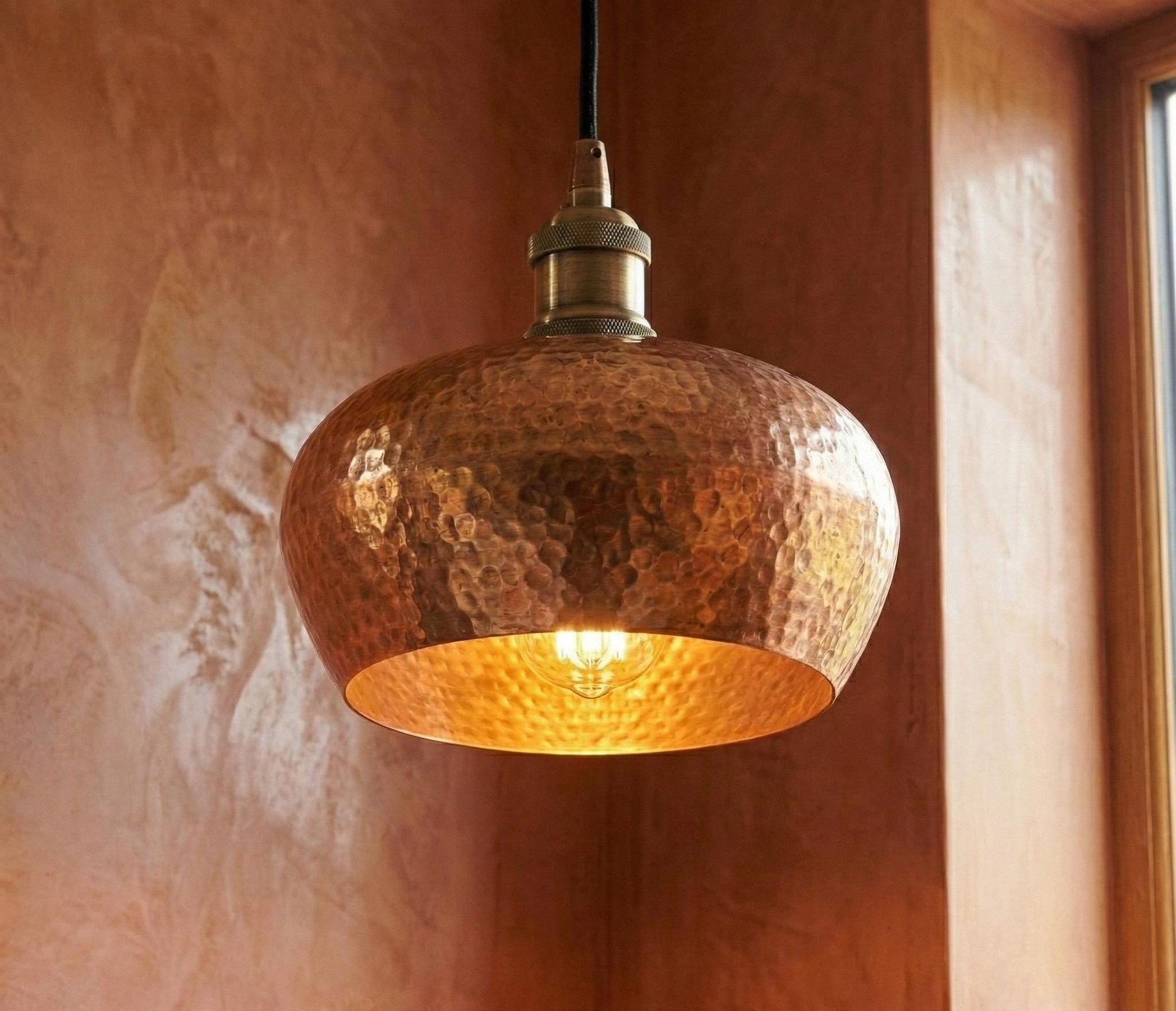 Copper pendant light hanging against a textured wall.