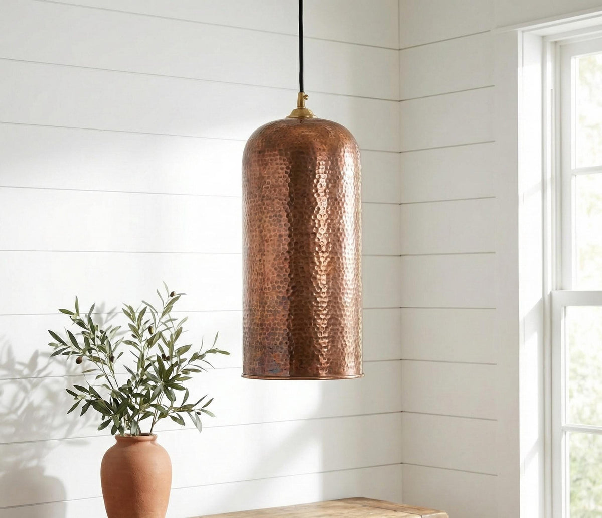 Copper pendant light hanging in a room with a plant and wooden surface.