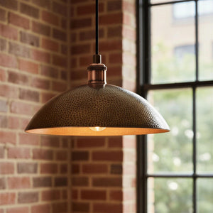 Hammered metal pendant light hanging against a brick wall with a window in the background