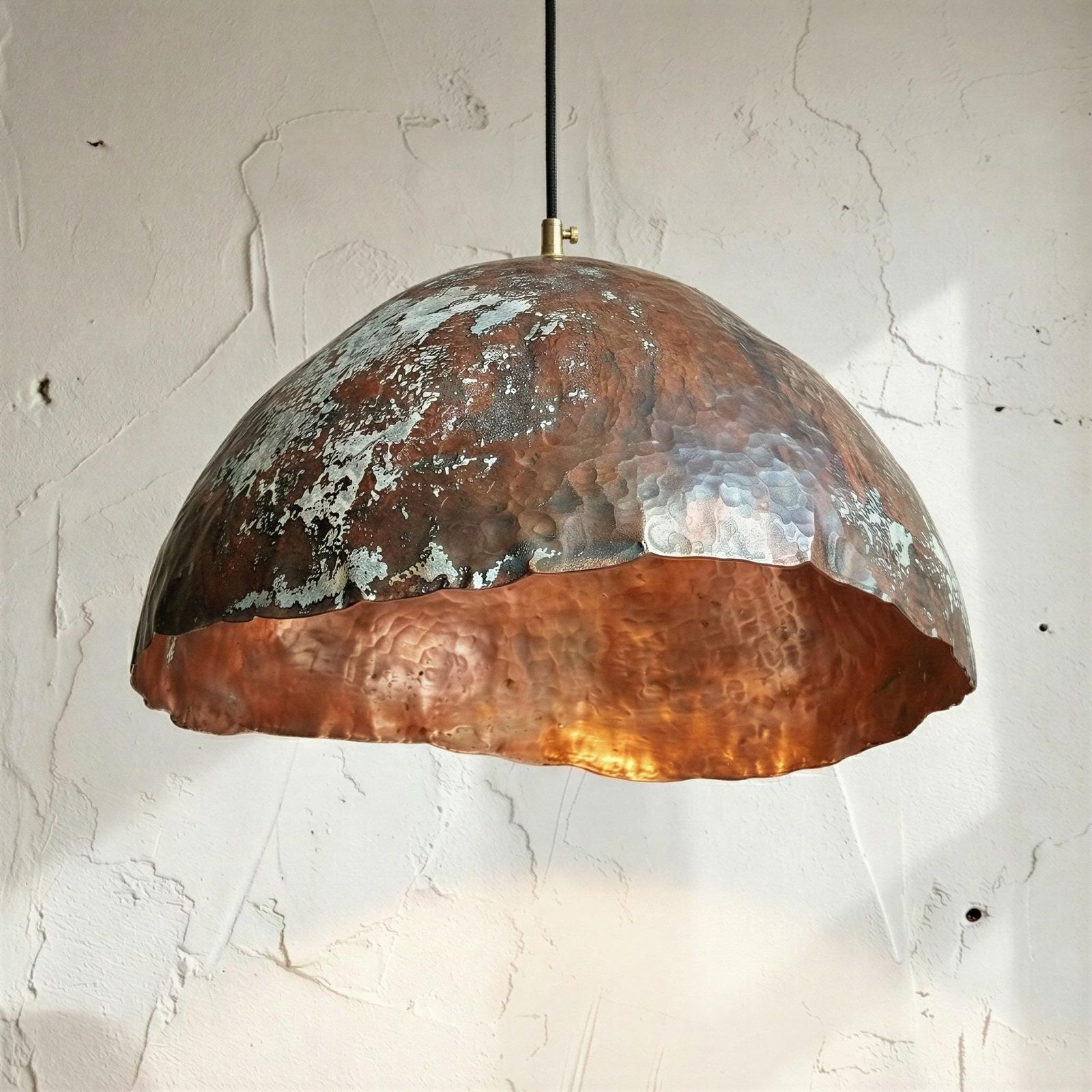 Copper pendant light hanging against a textured white wall
