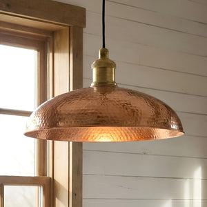 Copper pendant light hanging in a room with wooden window frame and white wall.