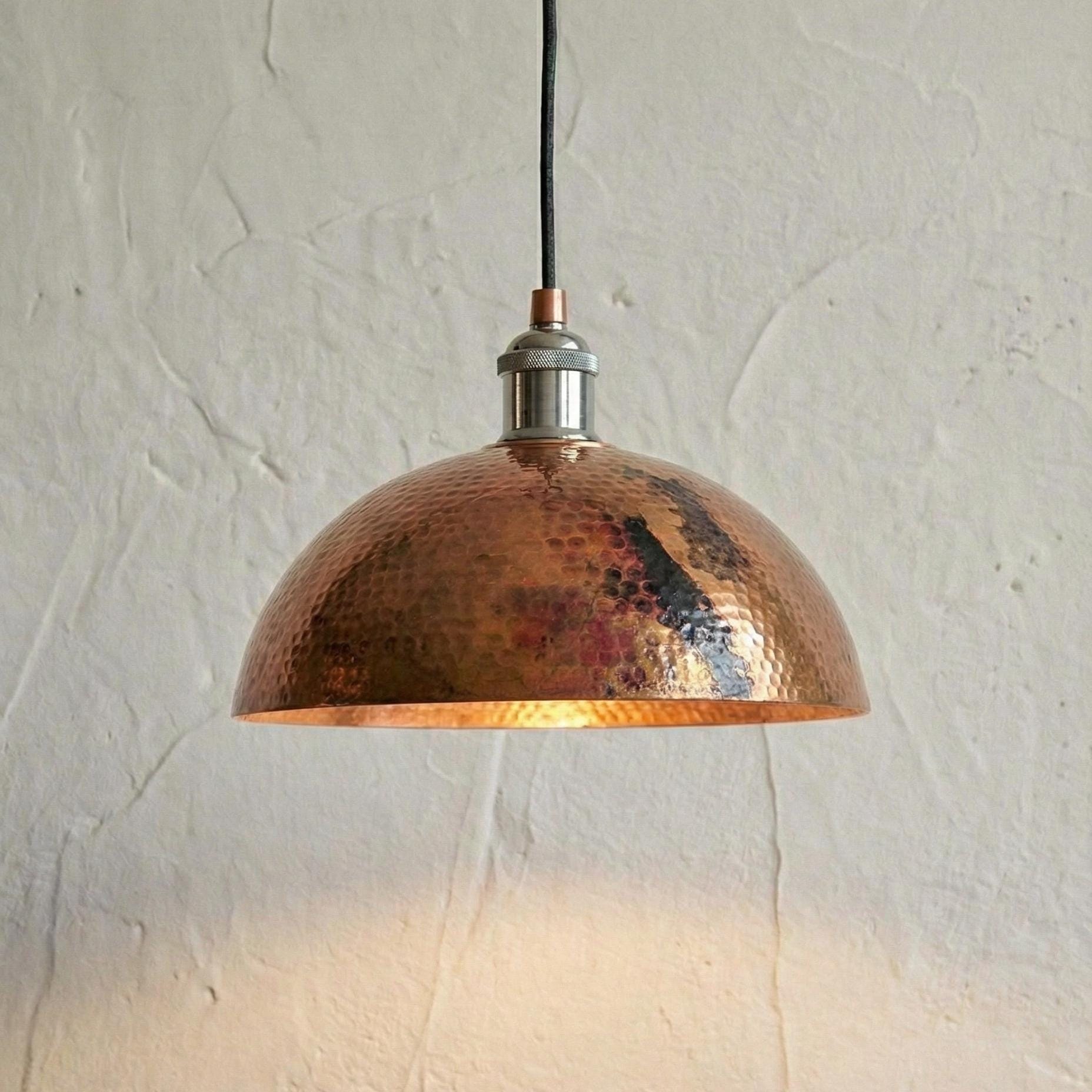 Copper pendant light hanging against a textured white wall