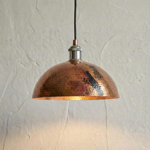 Copper pendant light hanging against a textured white wall
