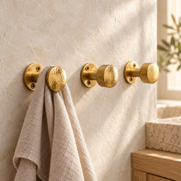 Hand-hammered solid brass wall hooks with linen towel on a plaster wall