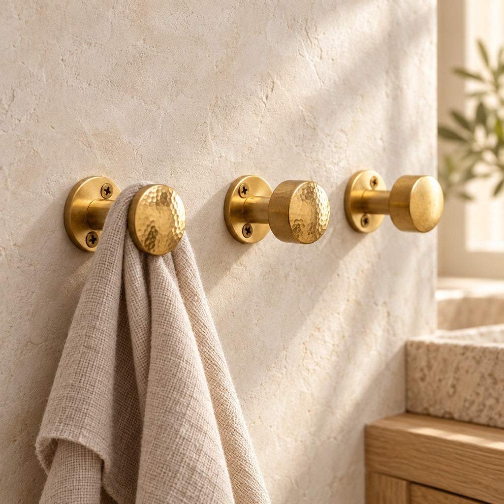 Hand-hammered solid brass wall hooks with linen towel on a plaster wall