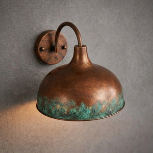 A vintage-style dome wall sconce with a distressed copper/bronze finish and turquoise verdigris patina along the lower rim, mounted on a textured gray wall.