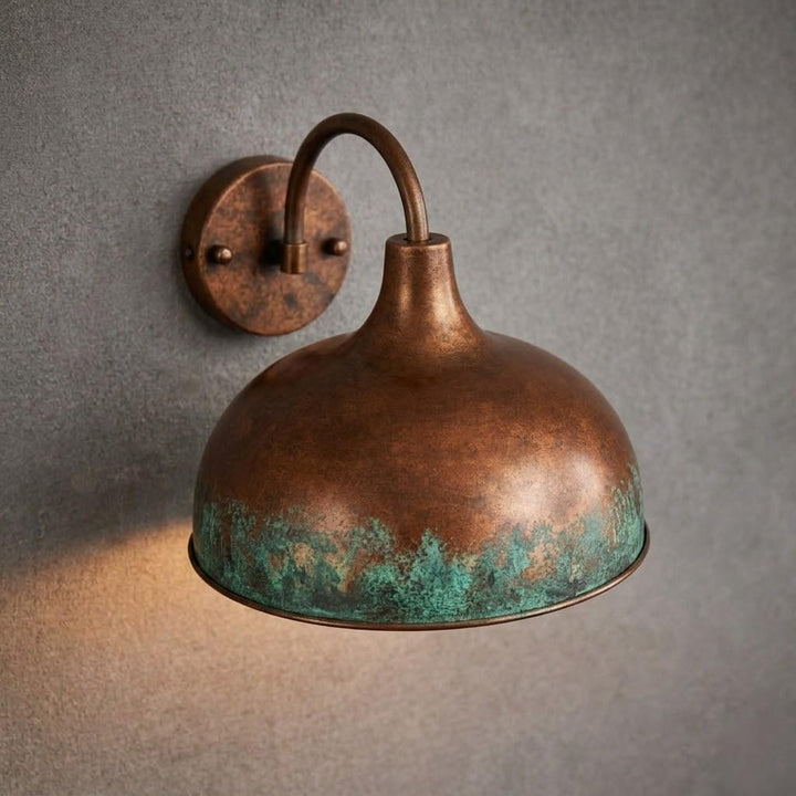 A vintage-style dome wall sconce with a distressed copper/bronze finish and turquoise verdigris patina along the lower rim, mounted on a textured gray wall.