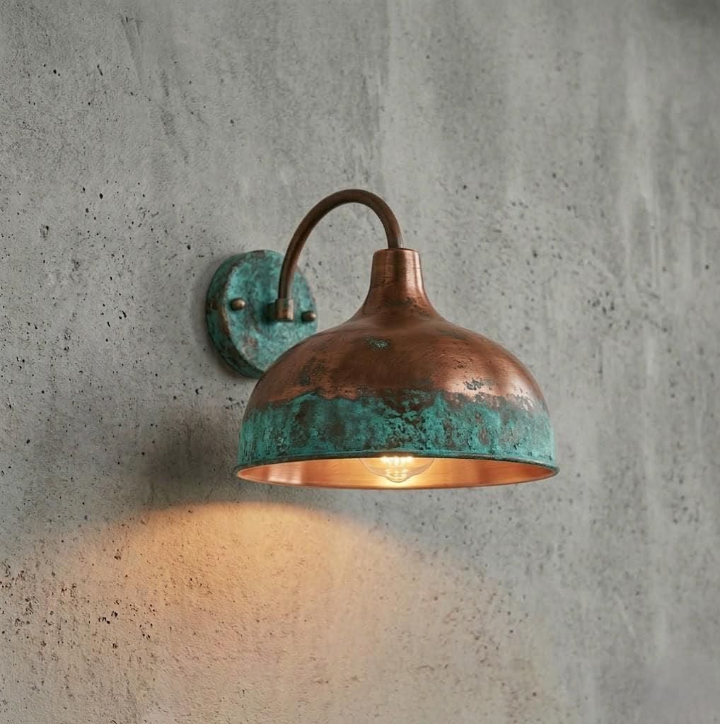 A copper dome wall sconce with a turquoise patina finish and a warm glowing light, mounted on a textured gray concrete wall.