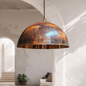 Rustic pendant light hanging in a room with white walls and a plant.