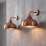 Two copper wall sconces with hammered textures mounted on a textured gray wall, casting a warm golden light downward.