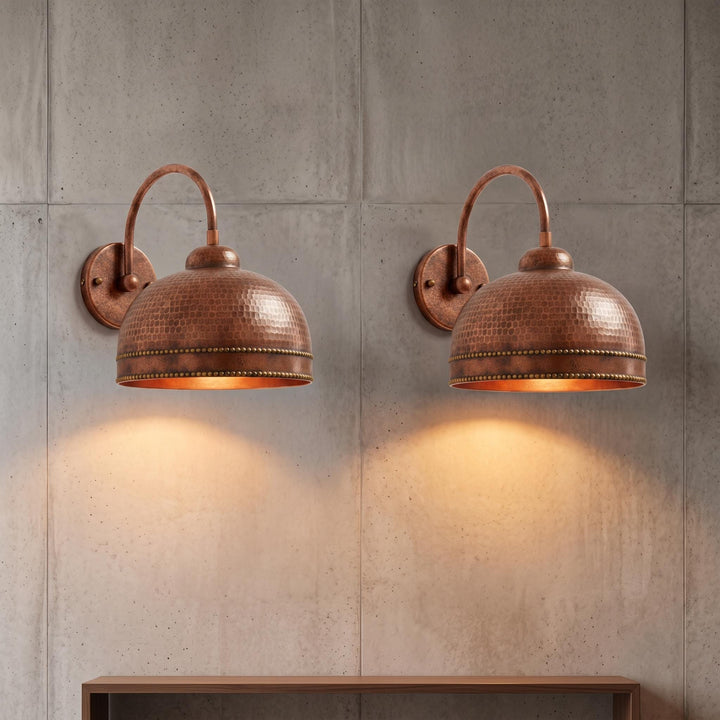 Two matching copper dome wall sconces mounted on a gray concrete wall, casting warm light downward.