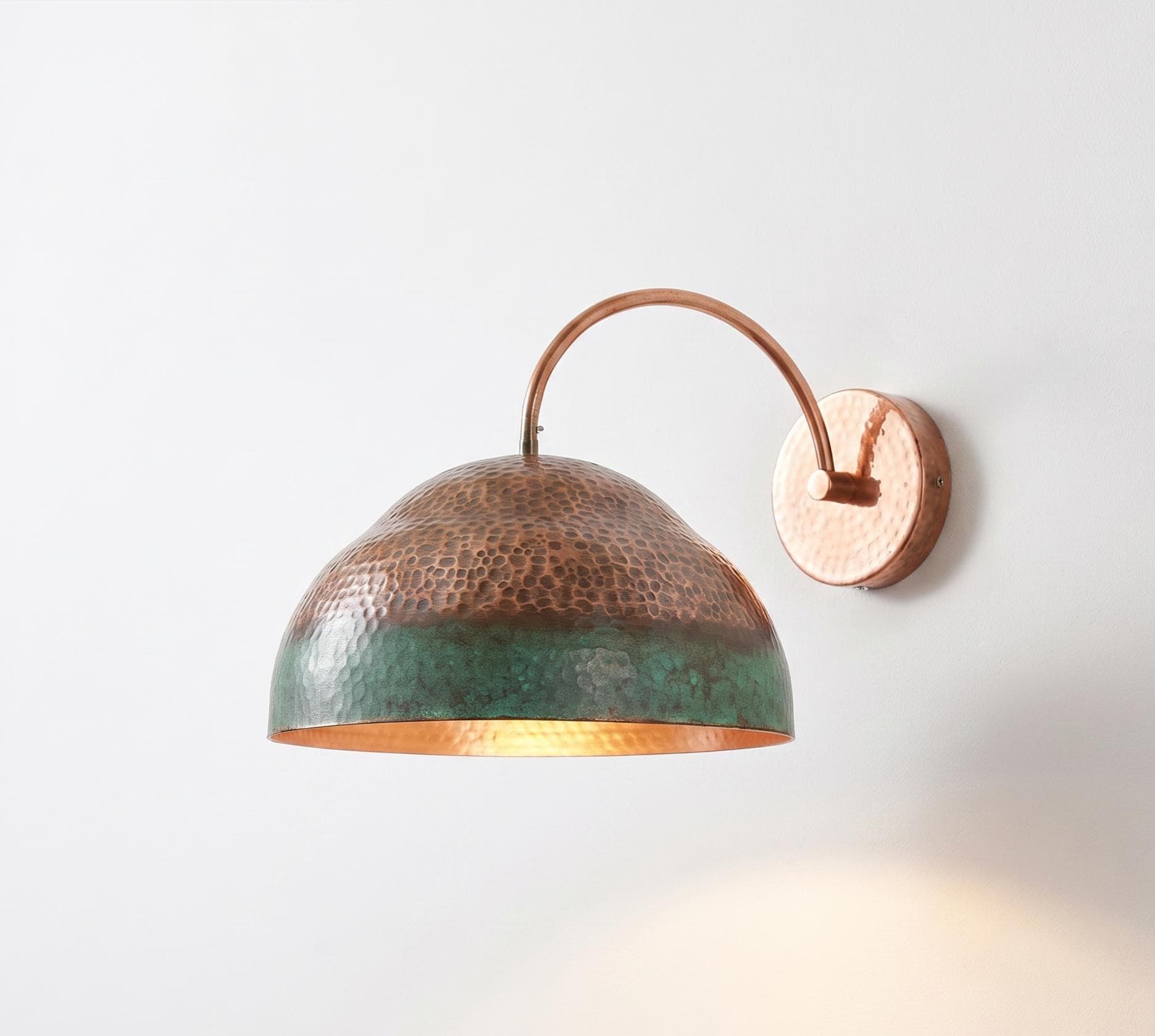 A hammered copper dome wall sconce with a green patina lower half and a warm copper-gold interior, mounted on a plain white wall.