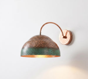 A hammered copper dome wall sconce with a green patina lower half and a warm copper-gold interior, mounted on a plain white wall.