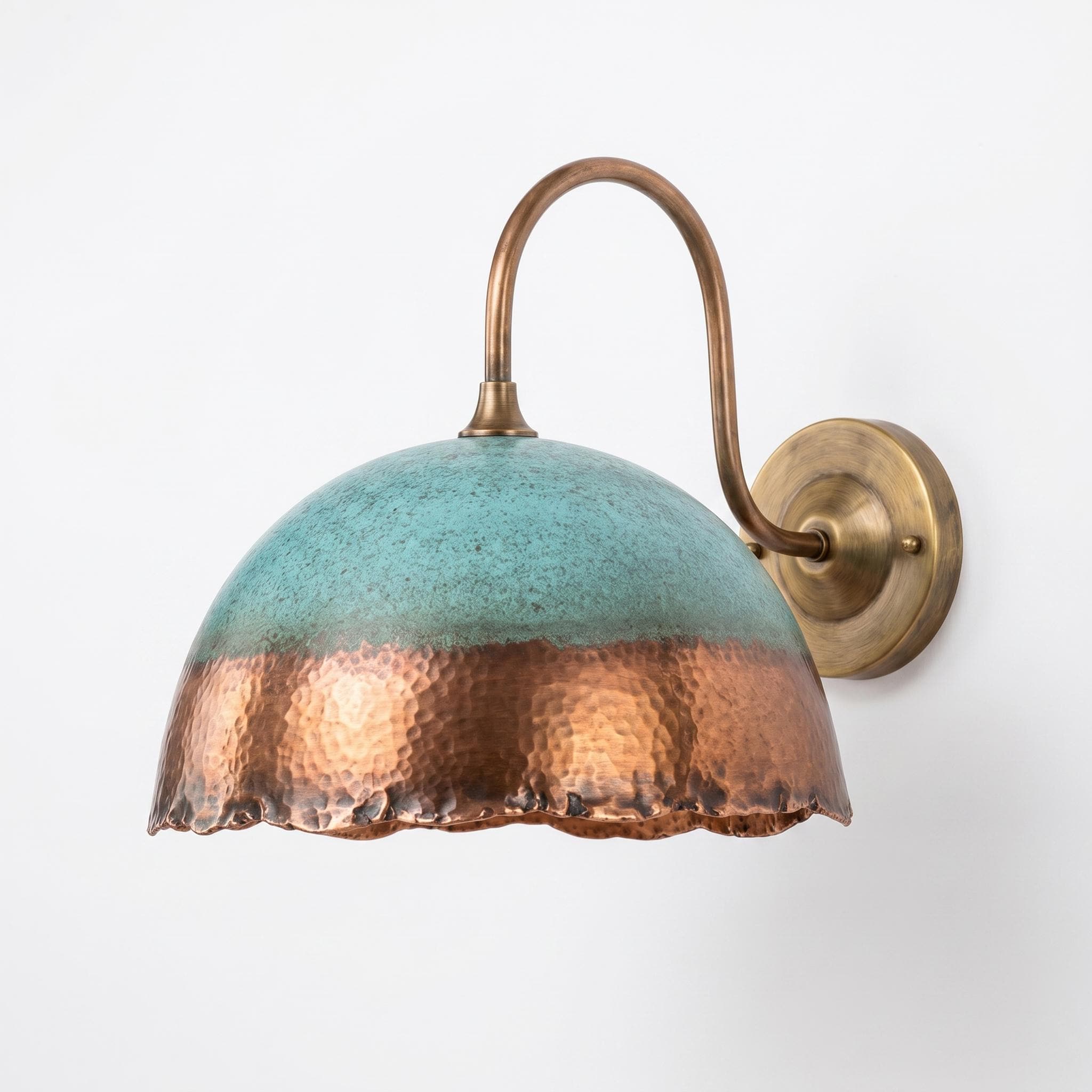 A wall-mounted sconce with a hammered dome shade featuring a two-tone finish of textured turquoise and copper, attached to a curved brass arm and round wall plate.