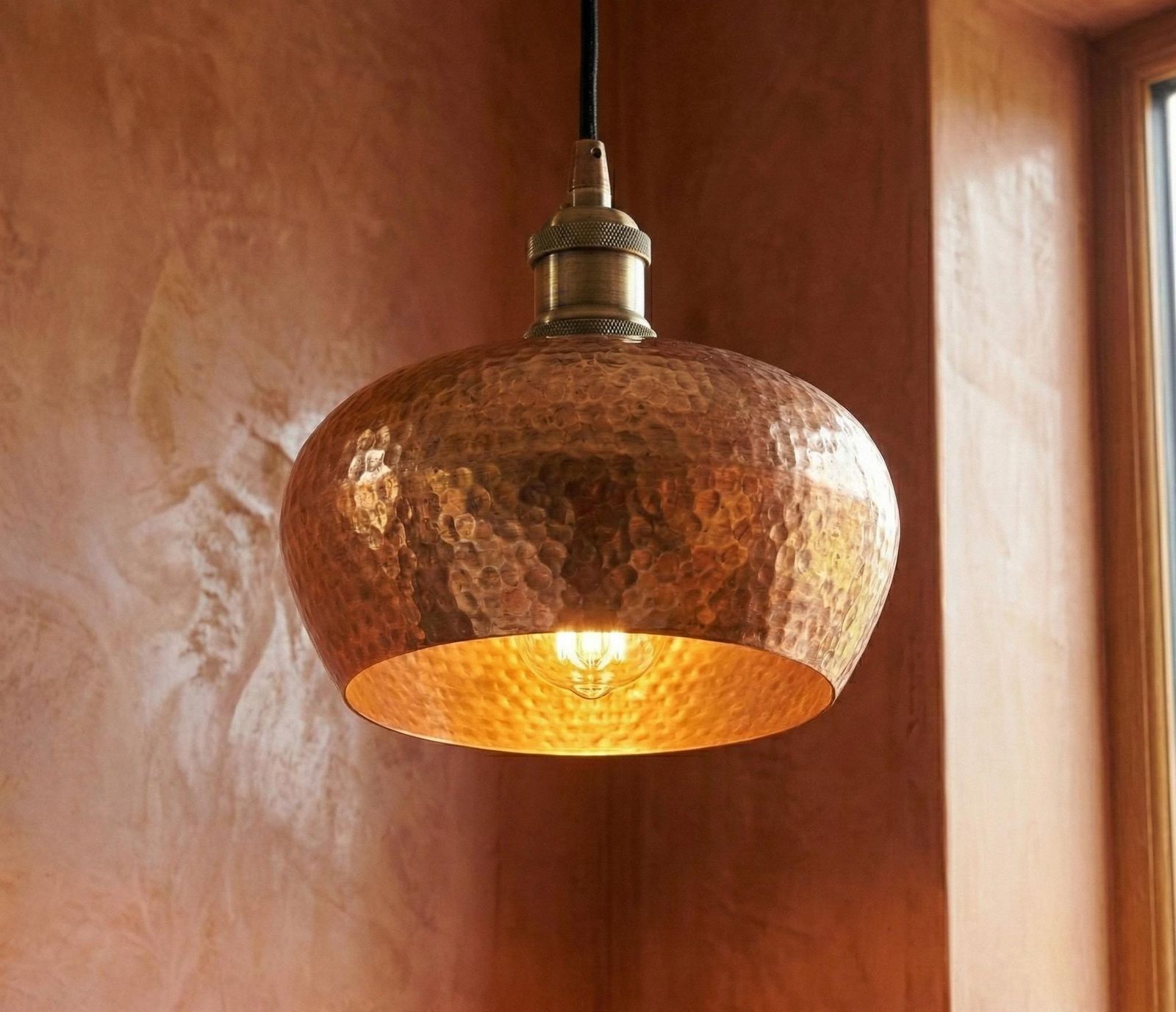 Copper pendant light hanging against a textured wall.