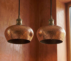 Two copper pendant lights hanging against a textured wall.
