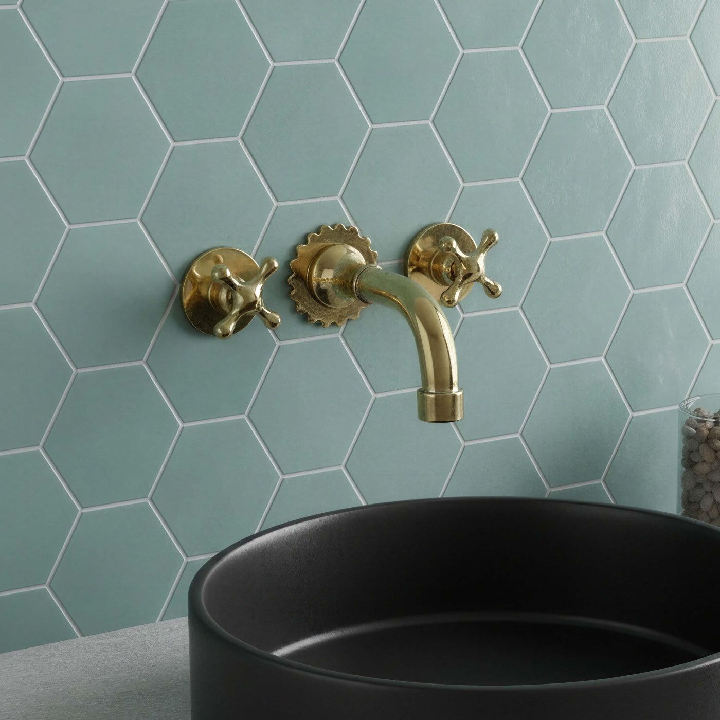 Gold faucet and handles on a light blue hexagonal tiled wall with a black sink.
